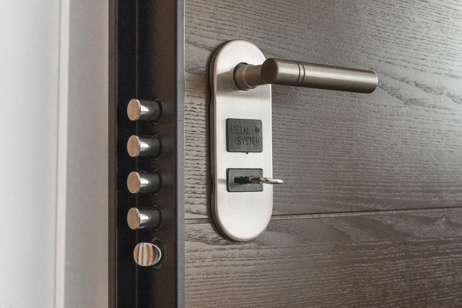 Steel door lever on an oval plate with a key in the lock, beside a row of metal bolts on the edge. — Caledon Village