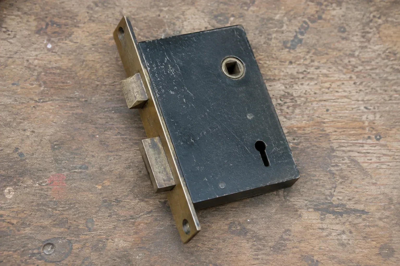 Closed mortise lock case with spindle opening, keyhole, latch and deadbolt on a wooden workbench. — Vintage Mortise Lock Service, Caledon
