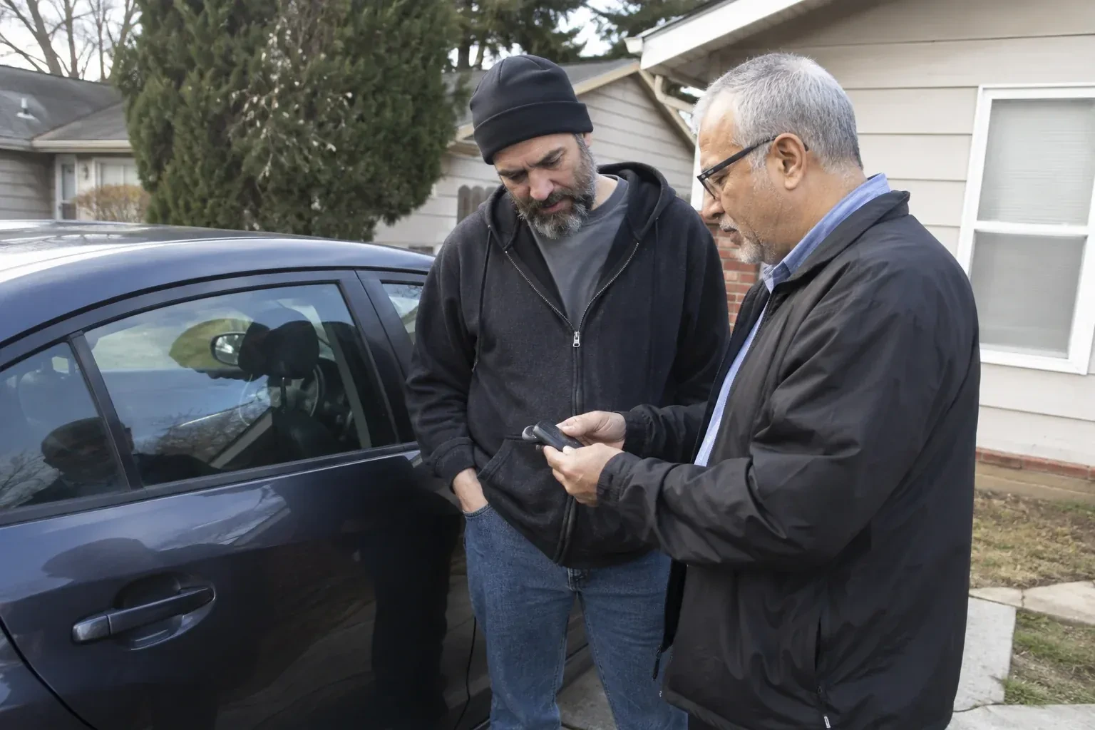 Two adults discussing a key fob beside a parked car. — Car Lockout Service, Caledon